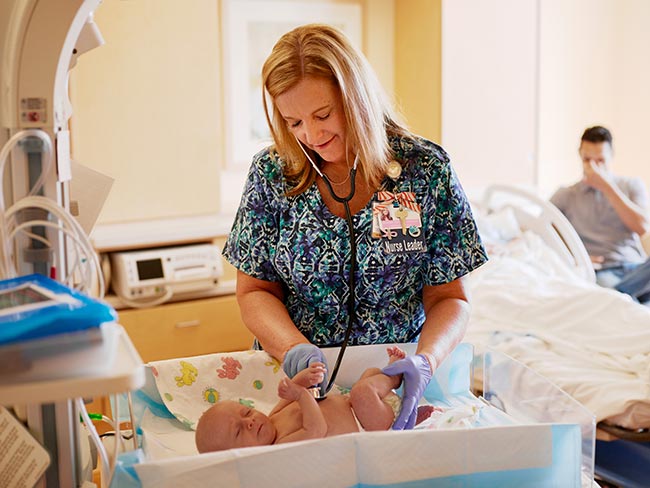 A smiling nurse listening to a newborn baby's heart with a stethoscope